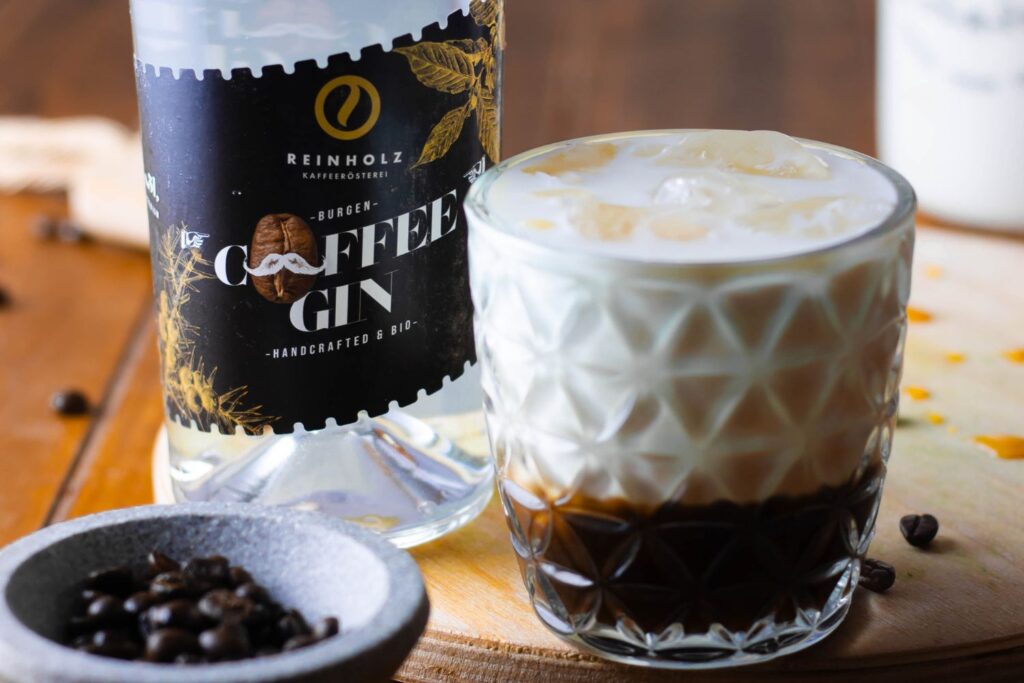 Flasche Coffee Gin neben einem Glas mit geschichteten Eis- und Kaffeemilchgetränk auf einem Holztisch.