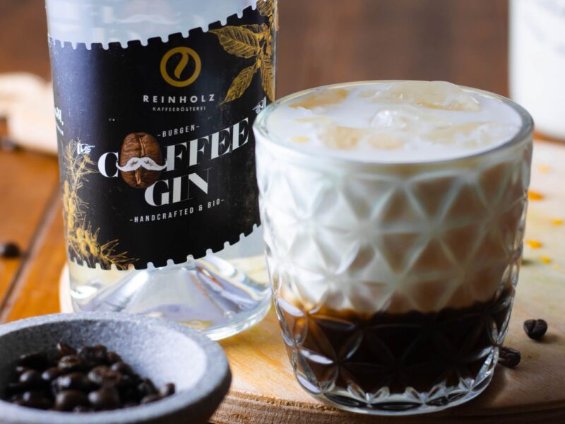 Flasche Coffee Gin neben einem Glas mit geschichteten Eis- und Kaffeemilchgetränk auf einem Holztisch.