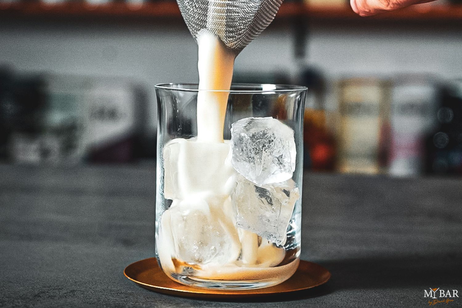 Cocktail wird durch ein Sieb auf Eiswürfel in einem Glas gegossen, auf einem Tisch stehend.