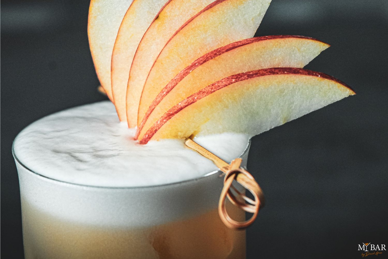 Cocktail mit Schaum, garniert mit aufgespießten dünnen Apfelscheiben.