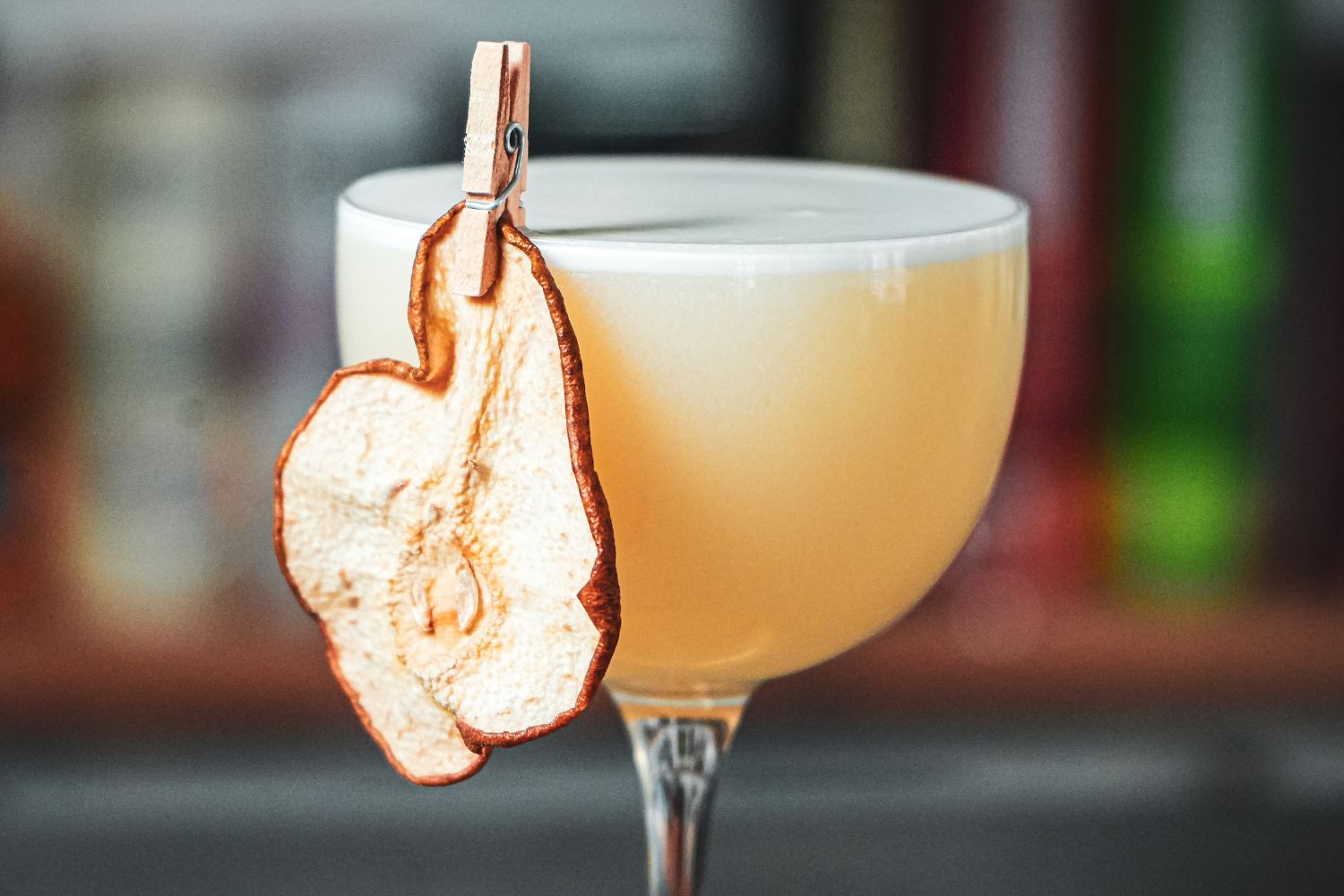 Cocktail im Glas mit Schaumkrone, garniert mit getrockneter Birne, befestigt mit einer kleinen Wäscheklammer.