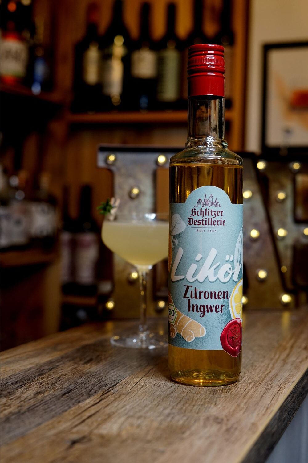 Miracle Elixier Flasche Zitronen-Ingwer-Likör der Schlitzer Destillerie auf Holztisch, im Hintergrund ein Cocktailglas.