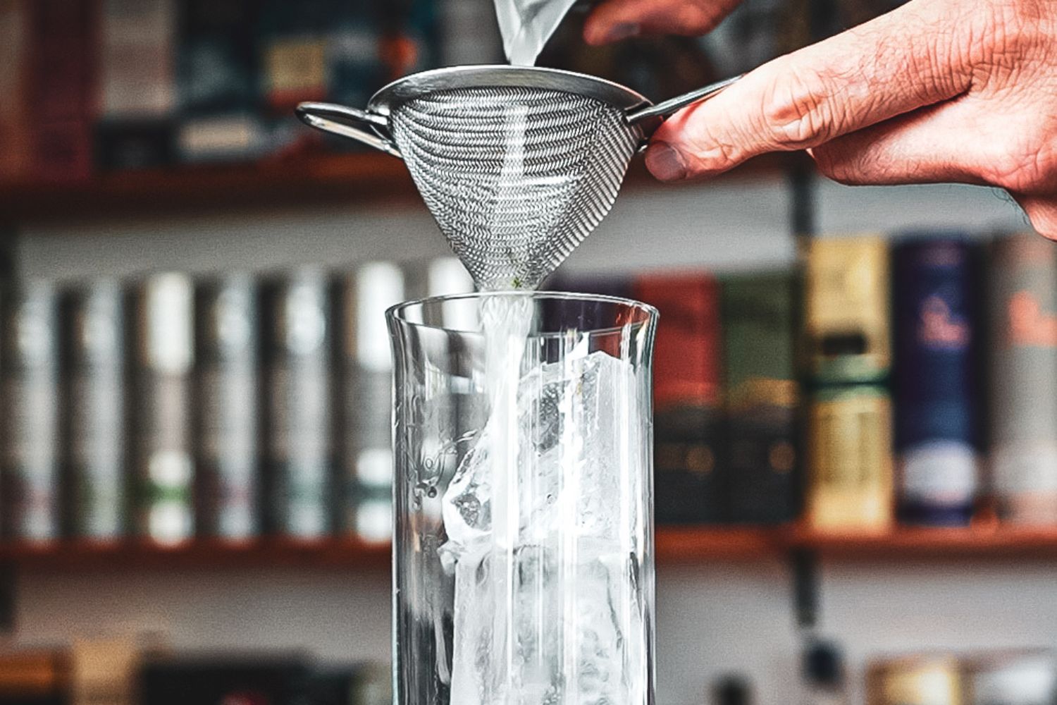 Flüssigkeit wird durch ein Sieb in ein Glas mit Eiswürfeln gegossen.