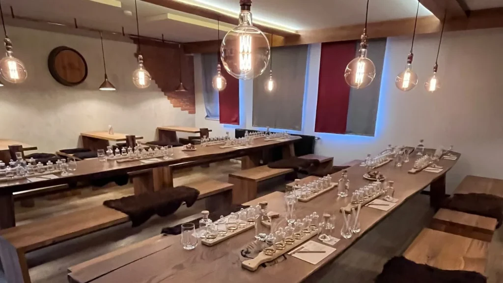 Verkostungssaal der Schlitzer Destillerie mit langen Eichentafeln, Bänken mit Fellen und Glühbirnen, eingedeckt für ein Whisky-Tasting