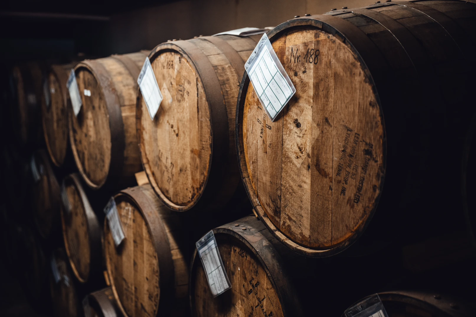 Historisches Whiskylager mit Holzfässern in der Schlitzer Destillerie Historisches Whisky-Lager der Schlitzer Destillerie mit Holzfässern in Reihen, gelagert in rustikaler Backsteinhalle mit warmem Licht