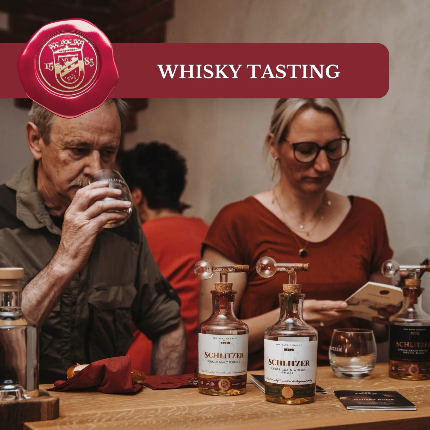 Whisky Tasting in der Schlitzer Destillerie – Erlebnisführung mit Verkostung Zwei Männer stehen in einem stimmungsvoll beleuchteten Lagerraum der Schlitzer Destillerie, umgeben von großen Holzfässern; sie riechen an einem Glas Whisky, was ein hochwertiges Whisky-Tasting und traditionelle Handwerkskunst vermittelt.