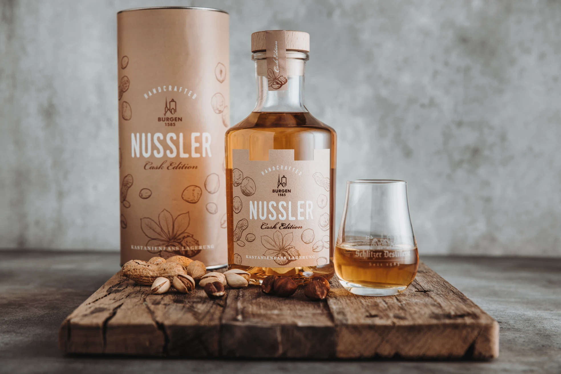 Schlitzer Destillerie Nussler Likör Produktbild 2022 Flasche Schlitzer Nussler Likör, umgeben von Nüssen auf einem Holztisch, hervorstechende braune Farbgebung des Likörs in klarem Glas, das traditionelle Design des Etiketts betont die handwerkliche Qualität und den regionalen Ursprung der Destillerie.