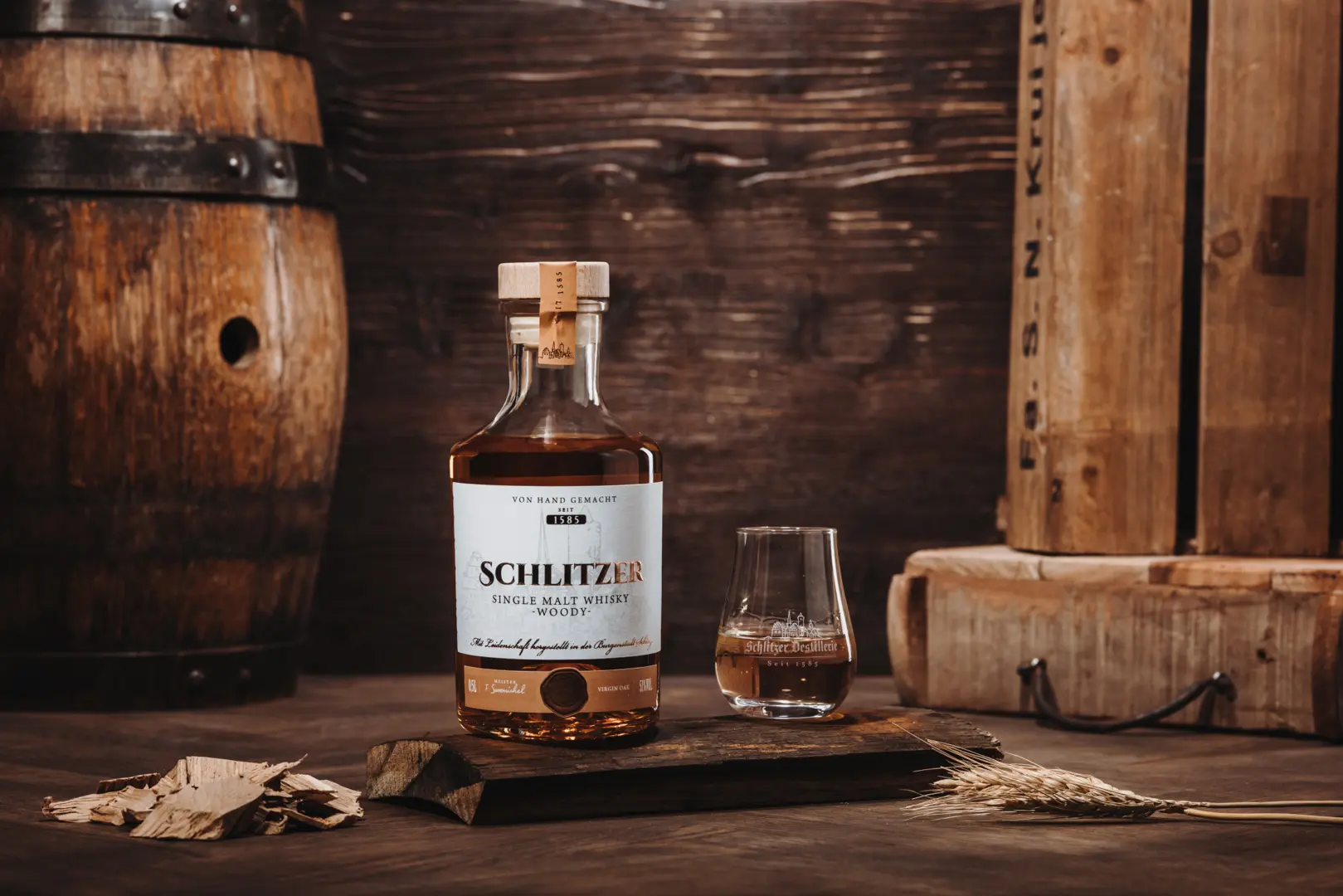 WOODY MOOD Likör – Edler Kräuterlikör in stilvoller Holzverpackung Flasche „Woody Mood“ Whiskey-Likör der Schlitzer Destillerie vor dunklem Holzhintergrund, daneben dekorative Holzscheiben und Wacholderzweige – edle Spirituose in stilvoller Naturpräsentation.