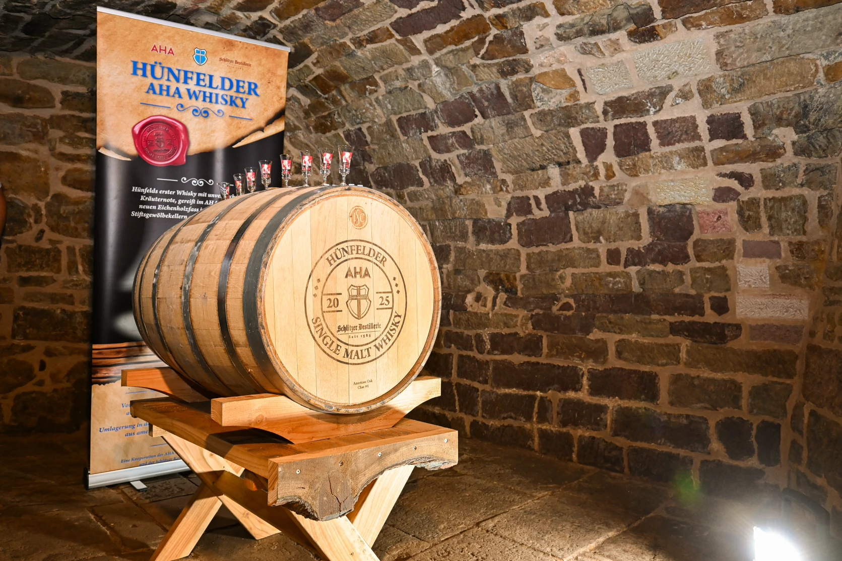 AHA Single Malt Whisky Tasting mit edlen Spirituosen in stilvollem Ambiente Vier stilvoll präsentierte Whiskyflaschen der AHA-Serie von Schlitzer Destillerie stehen nebeneinander auf einem Holzfass vor dunklem Hintergrund – jeweils mit individueller Farbkennzeichnung und AHA-Logo, ideal für Whisky-Tastings und Genießer hochwertig