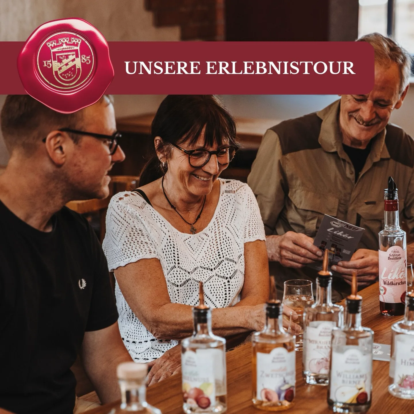 Schlitzer Erlebnistour – Führung durch die historische Destillerie in Hessen Zwei Männer in einem rustikalen Destillerie-Raum stoßen lachend mit Schnapsgläsern an; im Hintergrund traditionelle Holzfässer und Kupferbrennkessel der Schlitzer Destillerie – Erlebnistour durch historische Brennkunst.