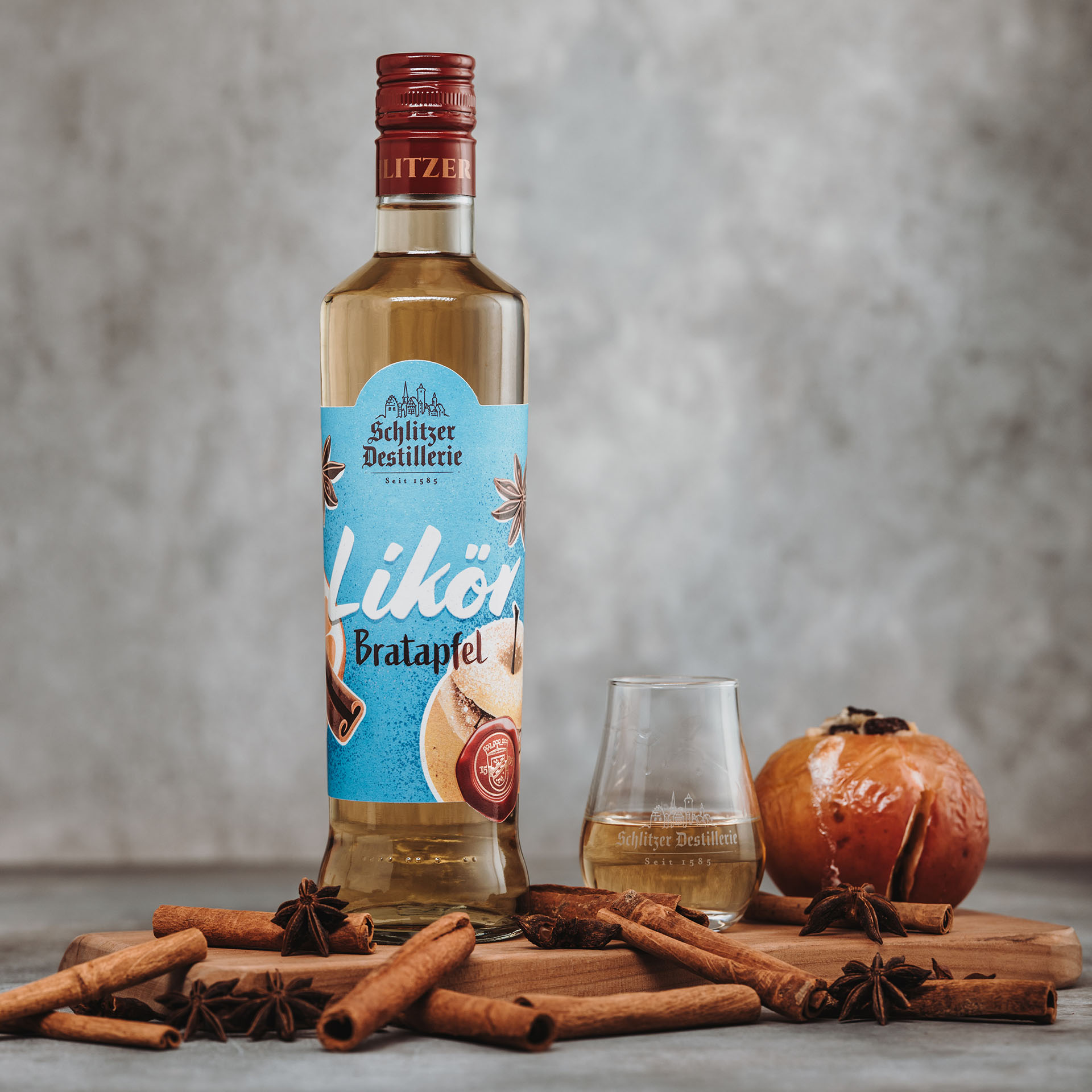 Bratapfellikör in stilvoller Flasche – Schlitzer Destillerie Spezialität Flasche Schlitzer Bratapfellikör vor weißem Hintergrund, goldene Flüssigkeit in bauchiger Flasche mit rotem Etikett, Aufschrift „Schlitzer Bratapfellikör“ und weihnachtlichen Designelementen.