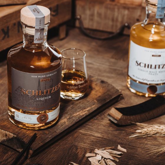 Whisky Likör in stilvoller Flasche mit goldenem Etikett – Schlitzer Destillerie Produktfoto Flasche Schlitzer Whisky Liqueur mit goldbrauner Flüssigkeit auf hellem Hintergrund, daneben Glas mit eingeschenktem Likör – deutsches Qualitätsprodukt mit edlem Design.