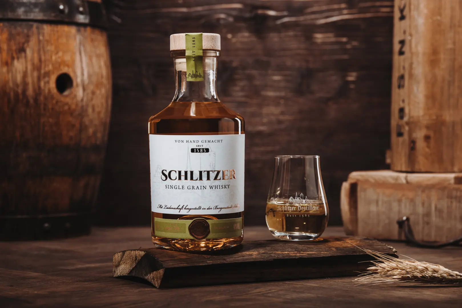 Schlitzer Grain Whisky – Deutscher Whisky in edler Flasche vor rustikalem Holzhintergrund Flasche Schlitzer German Whisky Grain auf Holztisch mit Glas, goldener Whisky leuchtend im Licht, hochwertige Verpackung im Hintergrund – deutscher Whisky aus der Schlitzer Destillerie.