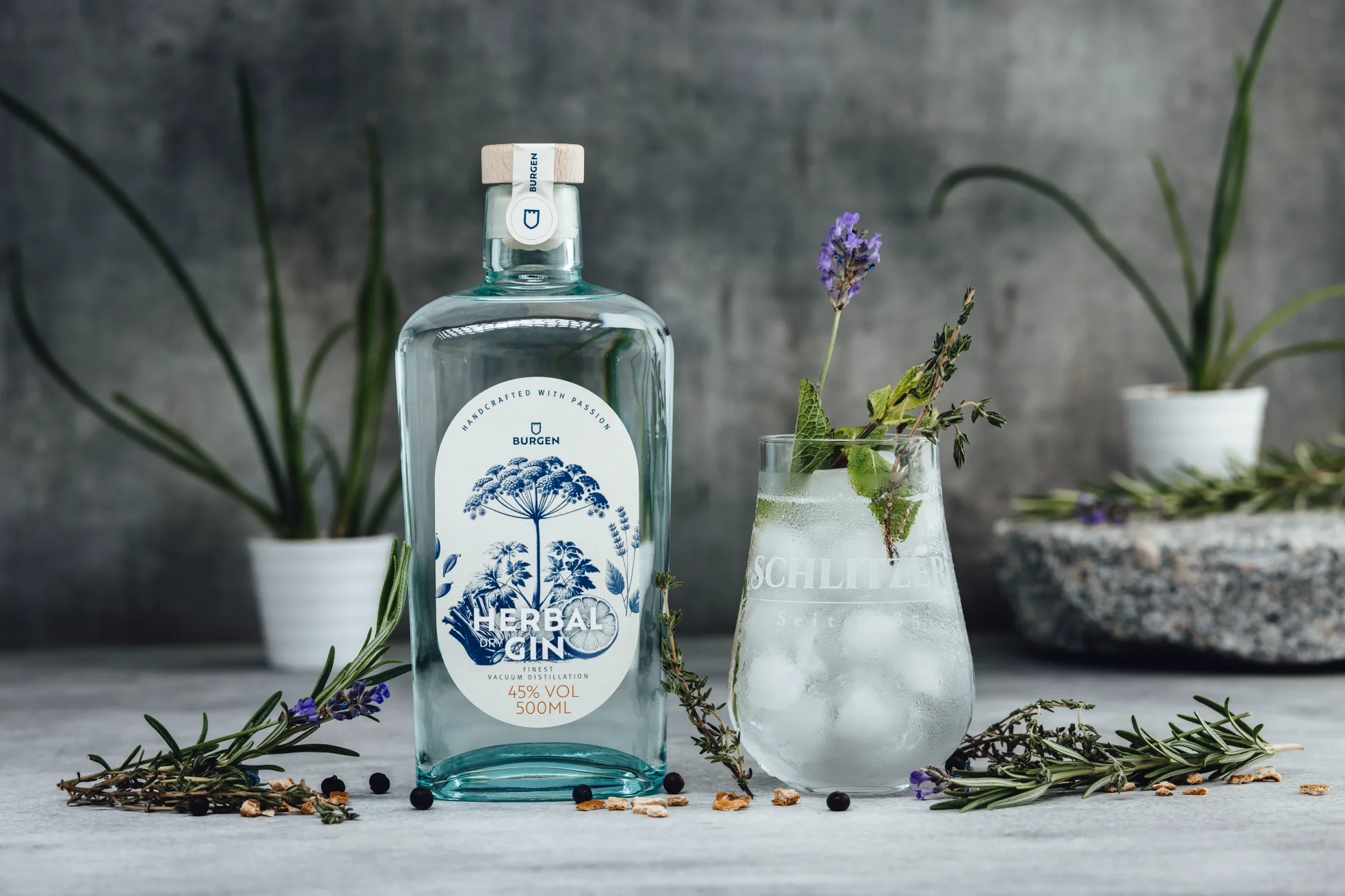 Schlitzer Bio Dry Gin – Premium Gin in ökologischer Glasflasche Klarglasflasche Schlitzer Bio Dry Gin mit blauem Etikett, dekorativ vor dunklem Hintergrund mit Wacholderbeeren und Botanicals arrangiert.