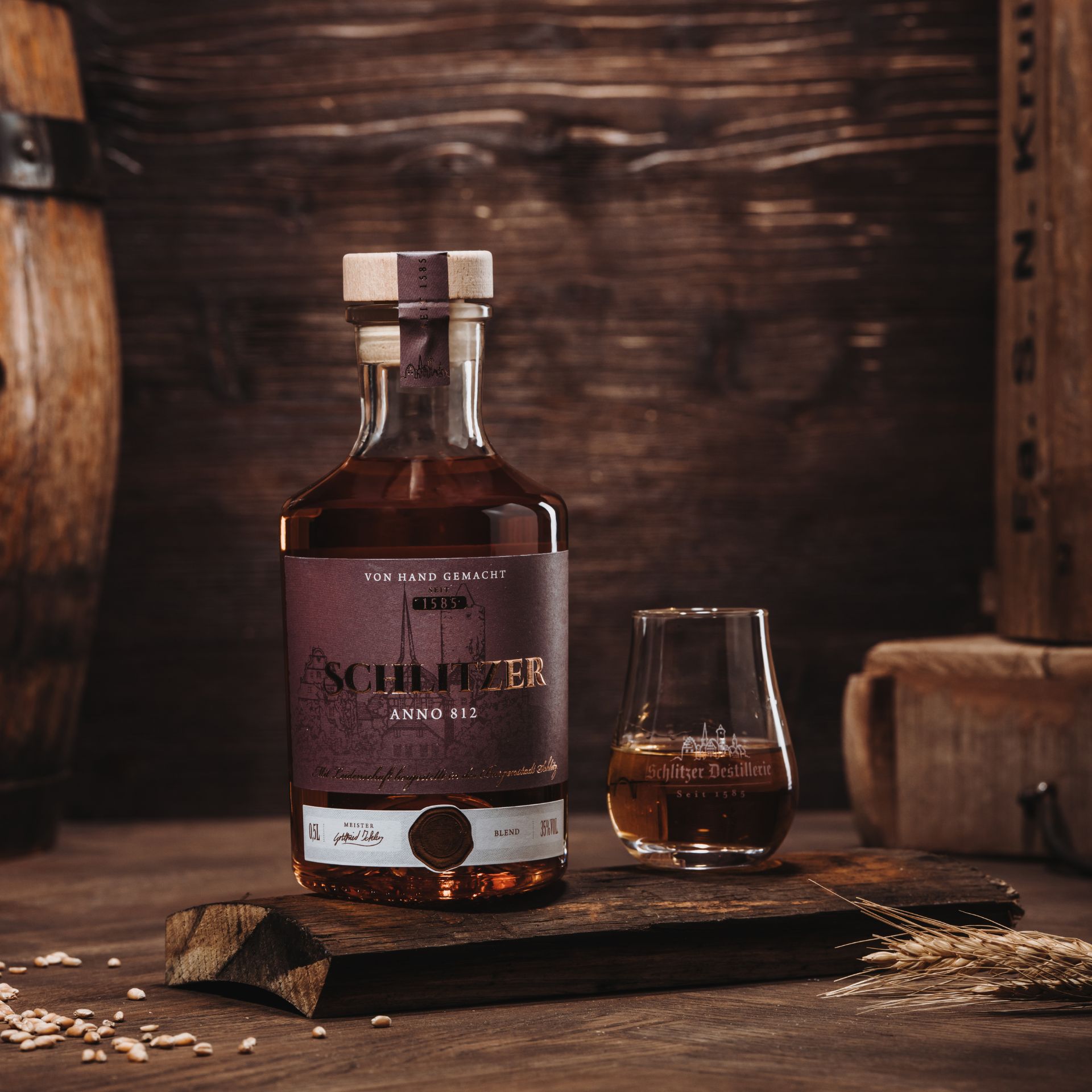 Flasche „Schlitzer Anno 812“ aus der Schlitzer Destillerie vor dunklem Hintergrund, edles Design mit goldener Schrift auf schwarzem Etikett, neben einem gefüllten Glas mit bernsteinfarbenem Edelbrand – hochwertiger deutscher Whisky in stilvoller Präsentat