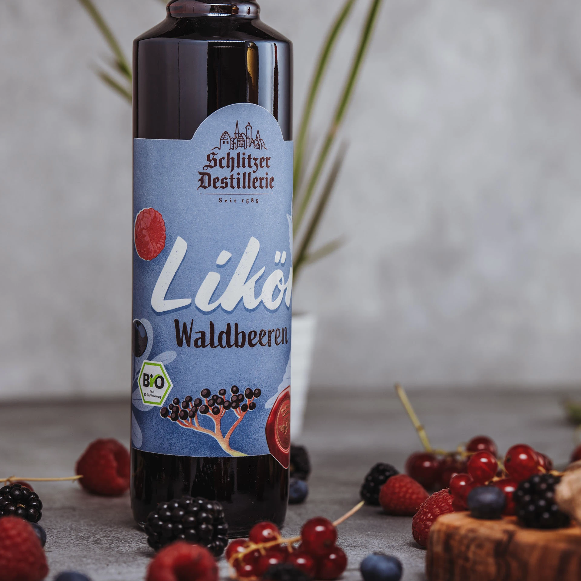 Bild des Waldbeeren Likörs der Schlitzer Destillerie in einer gläsernen Flasche mit rotem Etikett, umgeben von frischen Waldbeeren auf einem dunklen Hintergrund.