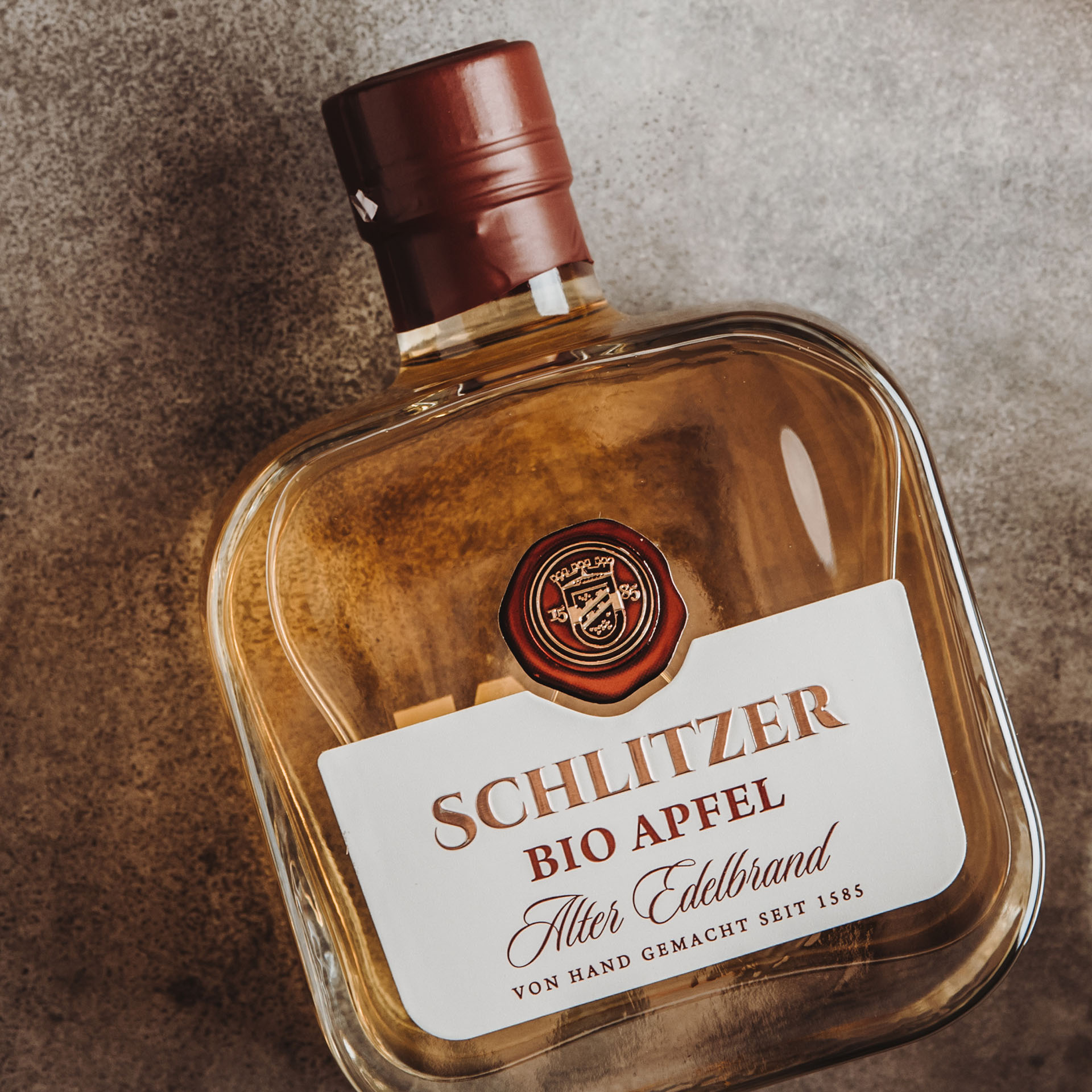 Alter Bio-Apfel-Brand Schlitzer Destillerie - Edles Obstbrandflair aus Deutschland Schlitzer Alter Bio-Apfel-Brand in eleganter Glasflasche vor hellem Hintergrund, präsentiert von der Schlitzer Destillerie. Perfekt für Liebhaber hochwertiger Bio-Spirituosen.