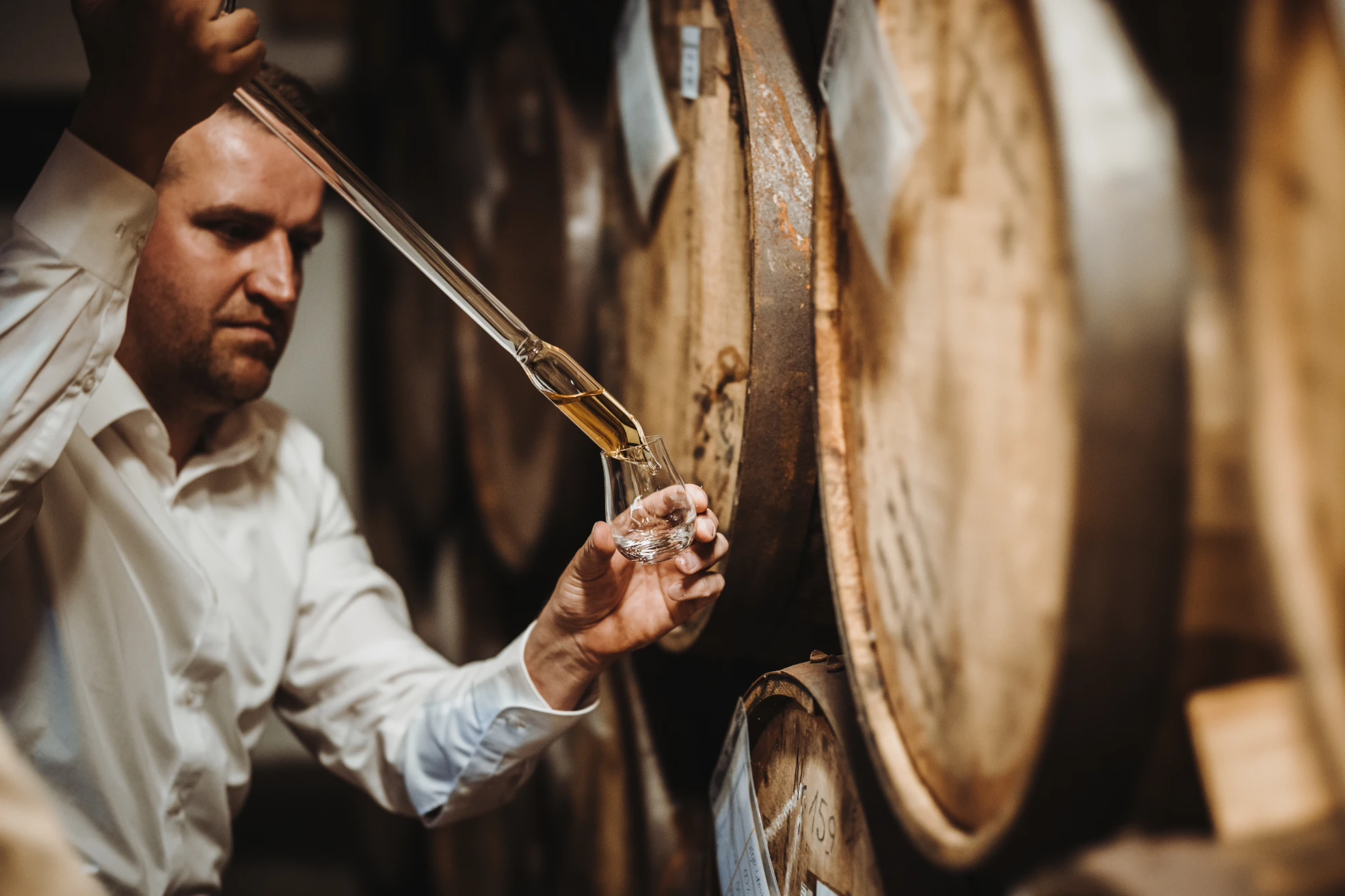 Whisky-Fassprobe in der Schlitzer Destillerie â Traditionelle Whiskyherstellung hautnah erleben Ein Mitarbeiter der Schlitzer Destillerie entnimmt mit einer Glasröhre eine Whisky-Probe aus einem Eichenfass in einem traditionellen Lagerkeller.