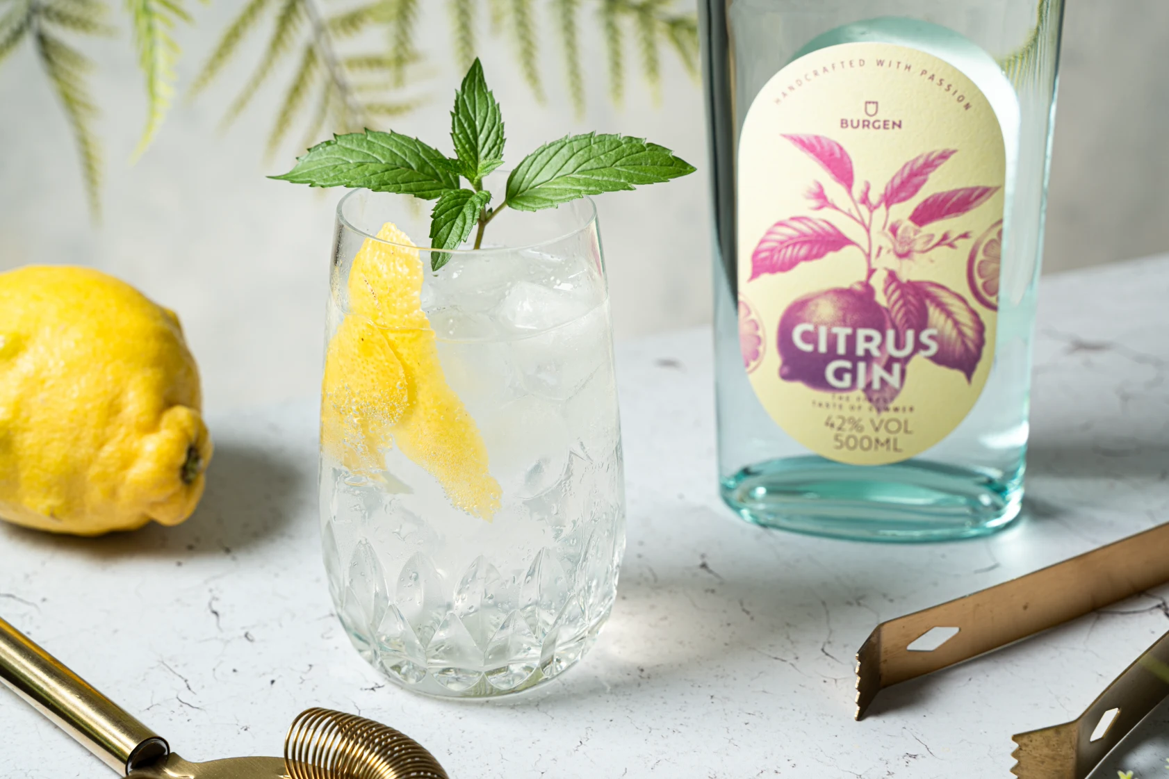Erfrischender Citrus Gin and Tonic mit Eis und Limettenscheiben im Glas Erfrischender Citrus Gin and Tonic in einem Glas mit Eiswürfeln, garniert mit einer Zitronenscheibe, daneben eine Citrus Gin Flasche der Schlitzer Destillerie auf einem Holztisch, im Hintergrund frische Zitronen und grünes Blattwerk.